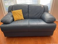 Front view of blue leather loveseat with yellow throw pillow