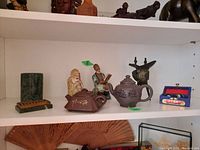 Overall shelf view showing both Yixing teapots, ceramic figures, stone vase, Baoding balls box and iron tripod stand