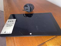 Microsoft Surface tablet laying flat with power charger coiled and placed above it on wooden table.