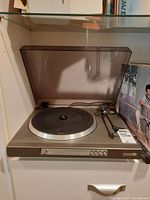 Front overview of Panta turntable with dust cover down in storage shelf with record nearby.