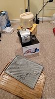 Two rice cookers placed on their respective boxes with two winter floor mats in foreground