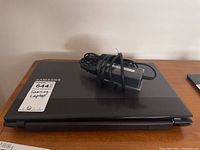 Closed black Samsung laptop with Samsung logo and MaxSold sticker on lid, charger placed on top.