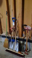 Wide view of all items showing the shovels, brooms, ice breaker, and small tool against wooden wall