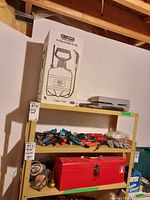 White RL FloMaster sprayer box with drawing and details on shelf with clamps, gloves, scissors, red toolbox, and other tools on metal shelves.