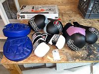 Lot of three pairs of gloves on wooden surface: blue padded target gloves, Combat Sports boxing gloves in black and white, and black-pink Hayabusa gloves.