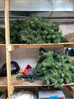 Artificial Christmas tree sections stored on shelves, showing green branches with integrated string lights, power cord and stand visible.