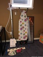 Full view of steamer, ironing board, wall mirror, iron, coat rack, and My Little Steamer Go Mini handheld steamer on floor