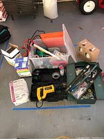 Overview of the lot showing DeWalt saw case, grout boxes, plastic bin with tools, metal toolbox, and lamps in boxes.
