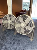 Two Holmes brand electric floor fans shown side by side on carpeted floor in room with furniture.