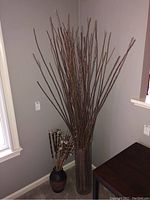 View showing both vases and planted faux branches and reeds against wall corner.
