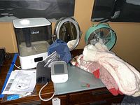 Full view of humidifier, fan, slippers, mirror, blood pressure monitor, and bathroom scale on a surface with manuals and accessories.