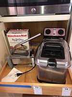 KitchenAid pasta roller and cutter set assembled and partially extended on wooden surface near fryer and French fry cutter with box behind.