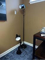 Full view of black metal floor lamp and smaller desk lamp with cords visible, placed in room corner