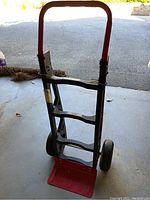 Front view of the hand truck showing the red handle and metal frame with wheels.