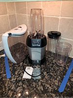 Nutri Ninja Pro BL456 blender base with attached tall mixing cup, two additional mixing cups, and Brita water pitcher on granite counter under tiled backsplash