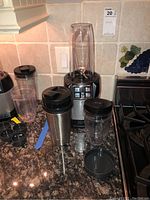 Photo showing Nutri Ninja Pro base unit with three cups including two plastic mixing cups and one metal travel cup. Lids are black, blending blade attached inside the base.