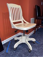 Full view of white wooden office chair showing slatted back, contoured seat, adjustable height lever, and caster wheels.