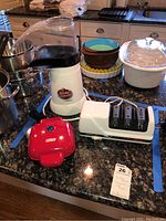 Full lot showing popcorn maker, knife sharpener, egg bite maker, other kitchenware pans and bowls on kitchen counter.