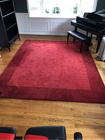 Full view of the Pottery Barn Woolmark red area rug on hardwood floor, showing the contrasting dark red border and lighter red center with visible edge wear.