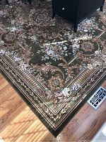 Close-up of corner edge showing green background with intricate floral and scrollwork design in brown and beige tones.