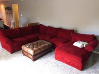 Overview of red sectional couch with four sections arranged in L-shape with blankets on chaise and brown ottoman in front