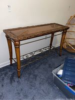 Full view of wooden sofa table with carved leaf patterns and metal shelf below.
