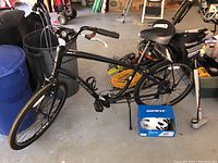 Matte black Trek bicycle with flat worn tires and accessories including a pump, headlight bag, and drink holder.