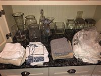 Full lot overview showing glass vases, jars, bottles on countertop and fold of towels and washcloths