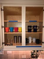 Cabinet shelves with four plastic cups, two rocks glasses, two Yeti tumblers, four ceramic coffee mugs including Baltimore Ravens mugs and others.