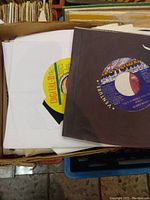 Photo of box with vintage 7-inch 45 RPM vinyl records, showing label details of Digital B and Motown records near top.