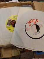 Close-up photo of vintage 45 RPM vinyl records showing paper sleeves and two visible record labels: Starlite label with Mel and Tim, and Nots label with John Holt.