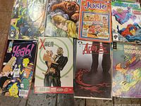 Photo showing seven vintage comic books with varied titles and colorful illustrated covers including Deadpool, Josie and the Pussycats, X-Men, After the Cape, Woody Woodpecker, and others.