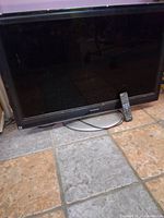 Front view of vintage Panasonic TV with remote placed at the base on tiled floor.