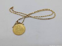 Overall view of 14k yellow gold twisted rope chain and pendant laid flat on white background
