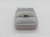 Ring displayed in grey velour ring box, front view showing three diamonds and yellow gold band