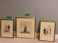Photo of three framed 19th century hand-coloured fashion engravings against a wall, two smaller on sides, one larger center