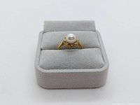 Front view of ring on grey display stand showing central pearl and scalloped bezel.
