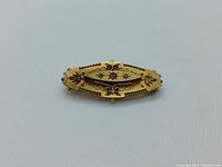 Top down photo of the yellow gold bar brooch showing detailed engraving and central red stone with diamonds.