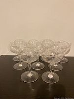 Nine clear cornflower etched glass champagne stemware glasses arranged in a group, showing etched floral patterns.