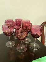 Eight cranberry glass wine glasses grouped together on a table showing their size and color.