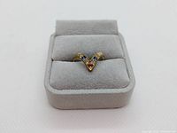 Front view of gold plated ring with V-shaped setting and five multicolored semi-precious stones in a grey jewelry box.