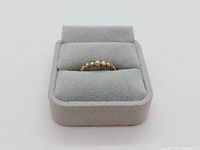 Front view of half seed pearl ring in grey velvet display box showing the pearls evenly spaced on gold band.