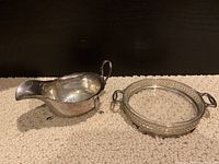 Photo of sterling silver sauce boat with handle and three legs, alongside sterling silver butter dish with pierced gallery and glass liner, shown on carpeted surface.