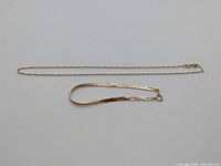 Flat link bracelet laid alongside delicate chain necklace on white background