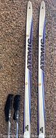 Atomic cross country skis and Elan ski poles laid on the ground showing skis with Atomic branding and poles with grips visible