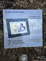 Photo of the sealed box of Pandigital 7-inch LCD Digital Photo Frame laid on natural ground with leaves and soil.