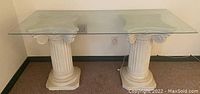 Full frontal image of the console table showing the glass top and two decorative classical column bases.