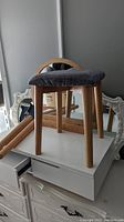 Matching stool with birch legs and cushioned gray fabric seat sitting on the makeup table.