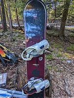 Front view of Rossignol snowboard with white bindings, showing the board standing upright outdoors on a tree stump.