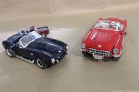 Front angle showing red 1957 Chevrolet Corvette and dark blue 427 AC Cobra model cars side by side